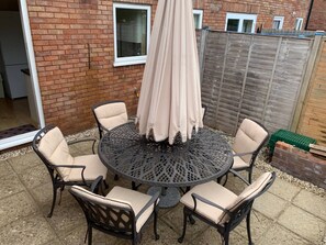 A round outdoor table with six chairs, surrounded by a brick wall and a wooden fence. - Beautiful home near to Musgrove Park Hospital (Taunton)