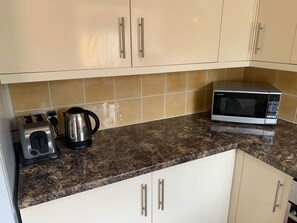 A kitchen with beige cabinets, a granite countertop, a toaster, a kettle, and a microwave. - Beautiful home near to Musgrove Park Hospital (Taunton)