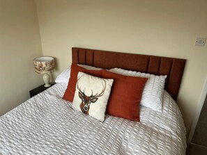 A neatly made bed with a patterned bedspread, a brown headboard, and decorative pillows including one with a deer head.