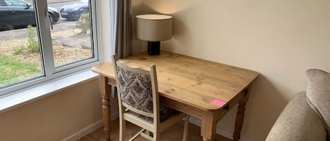 A room with a wooden table, a chair, a lamp, and a window overlooking a street.