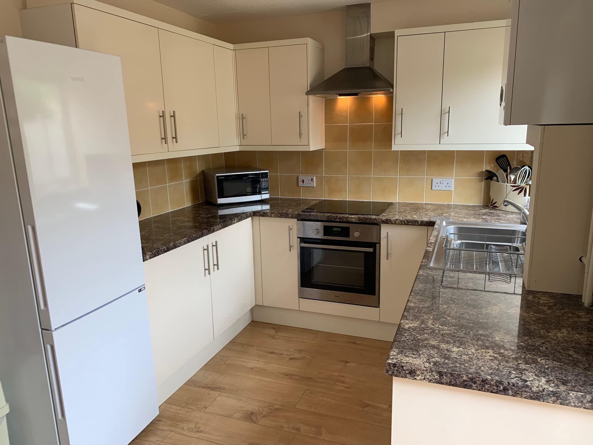 A compact kitchen with white cabinets, a microwave, an oven, and a stainless steel range hood.