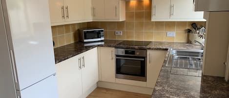 A compact kitchen with white cabinets, a microwave, an oven, and a stainless steel range hood.