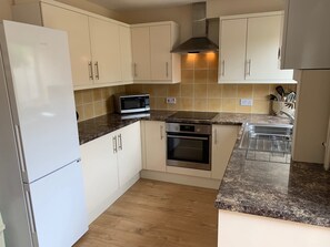 A compact kitchen with white cabinets, a microwave, an oven, and a stainless steel range hood. - Beautiful home near to Musgrove Park Hospital (Taunton)
