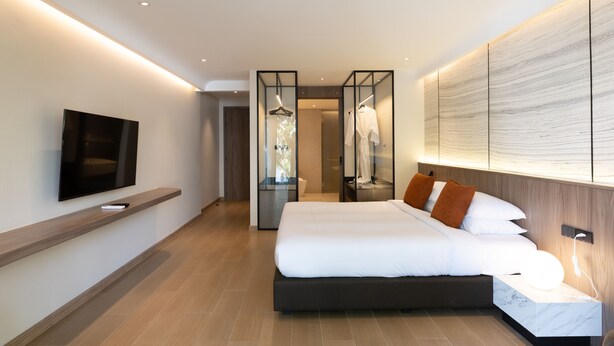 A modern hotel room with a large bed, a TV mounted on the wall, and a walk-in closet. - 5min to Beach/Bangla - Luxury 3BR Townhome + Pool (ตำบลป่าตอง)