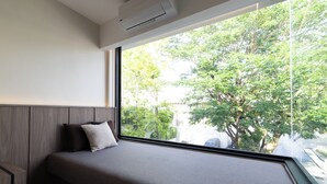 A modern bedroom with a large window, a bed with a grey mattress and pillows, and a wooden headboard. - 5min to Beach/Bangla - Luxury 3BR Townhome + Pool (ตำบลป่าตอง)