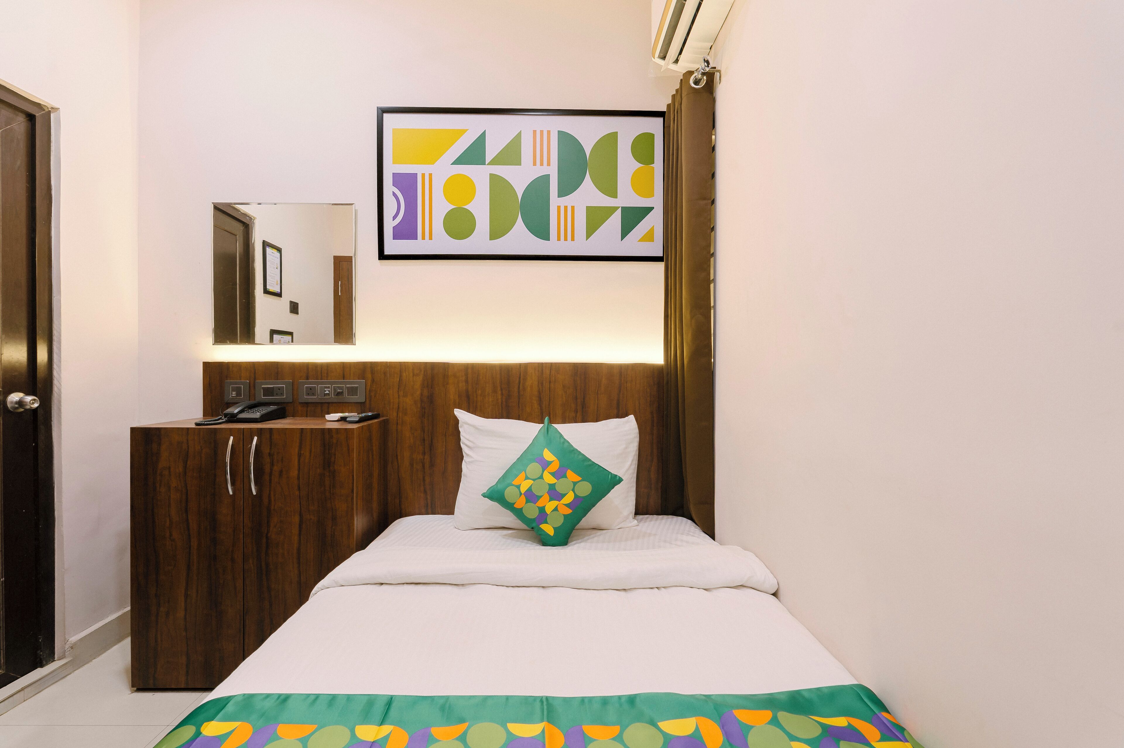 Habitación de hotel con una cama, un armario de madera, un espejo y una obra de arte abstracta enmarcada en la pared.