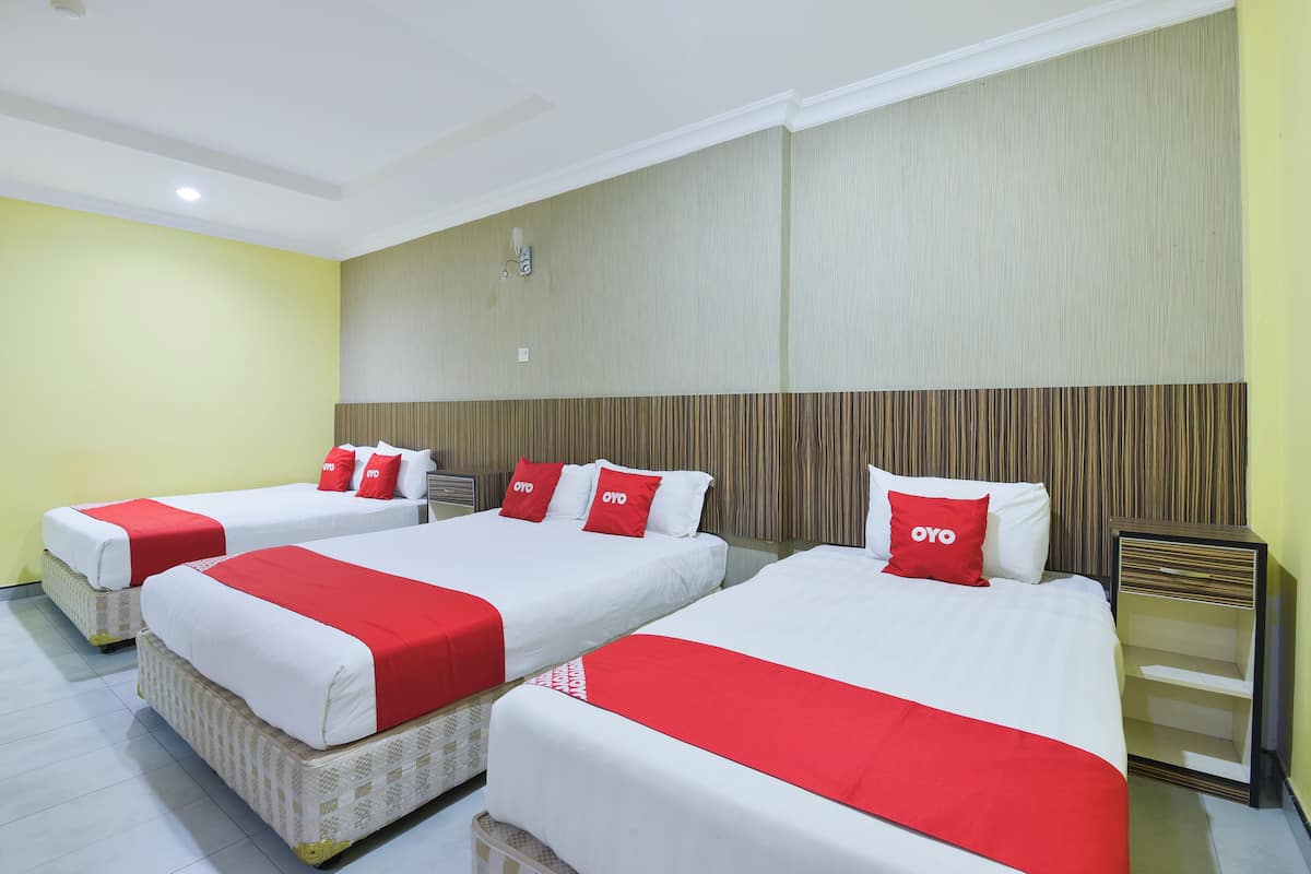 Ein Hotelzimmer mit drei Betten, jeweils mit weißer Bettwäsche und roten Akzenten, und einem hölzernen Kopfteil.