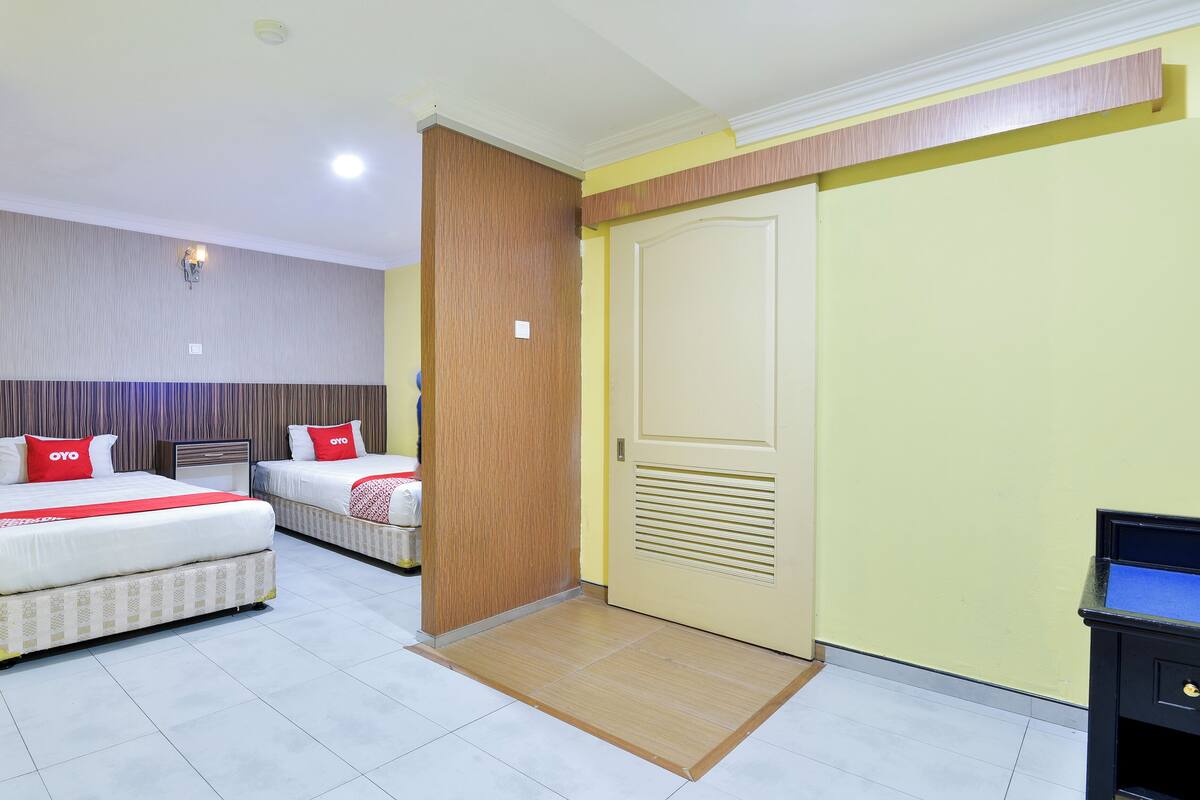 Ein Hotelzimmer mit zwei Betten, einem Holzschrank, einer Tür mit Lüftungsgitter und einem kleinen Schreibtisch mit Schubladen.