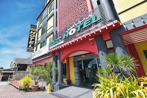 A hotel with a prominent sign, a red and yellow facade, and a paved entrance area with potted plants. - Hotel O Rayyan Soffea Managed by Oravel (Kota Bharu)