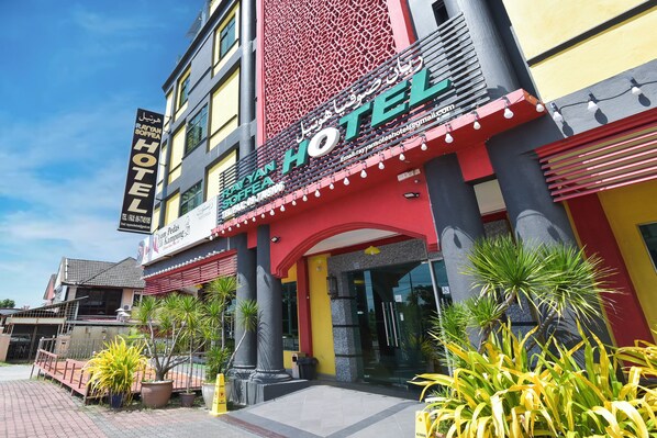 A hotel with a prominent sign, a red and yellow facade, and a paved entrance area with potted plants. - Hotel O Rayyan Soffea Managed by Oravel (Kota Bharu)