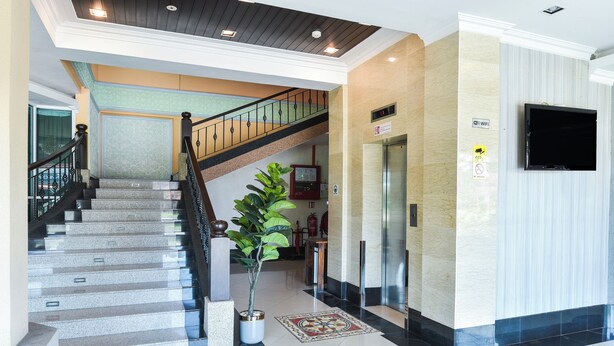 A hotel lobby with a staircase, a reception desk, a large potted plant, and a flat-screen TV mounted on the wall. - Hotel O Rayyan Soffea Managed by Oravel (Kota Bharu)