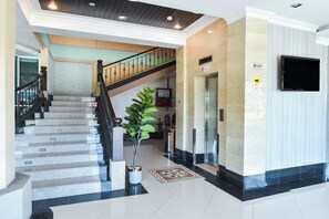 A hotel lobby with a staircase, a reception desk, a large potted plant, and a flat-screen TV mounted on the wall. - Hotel O Rayyan Soffea Managed by Oravel (Kota Bharu)