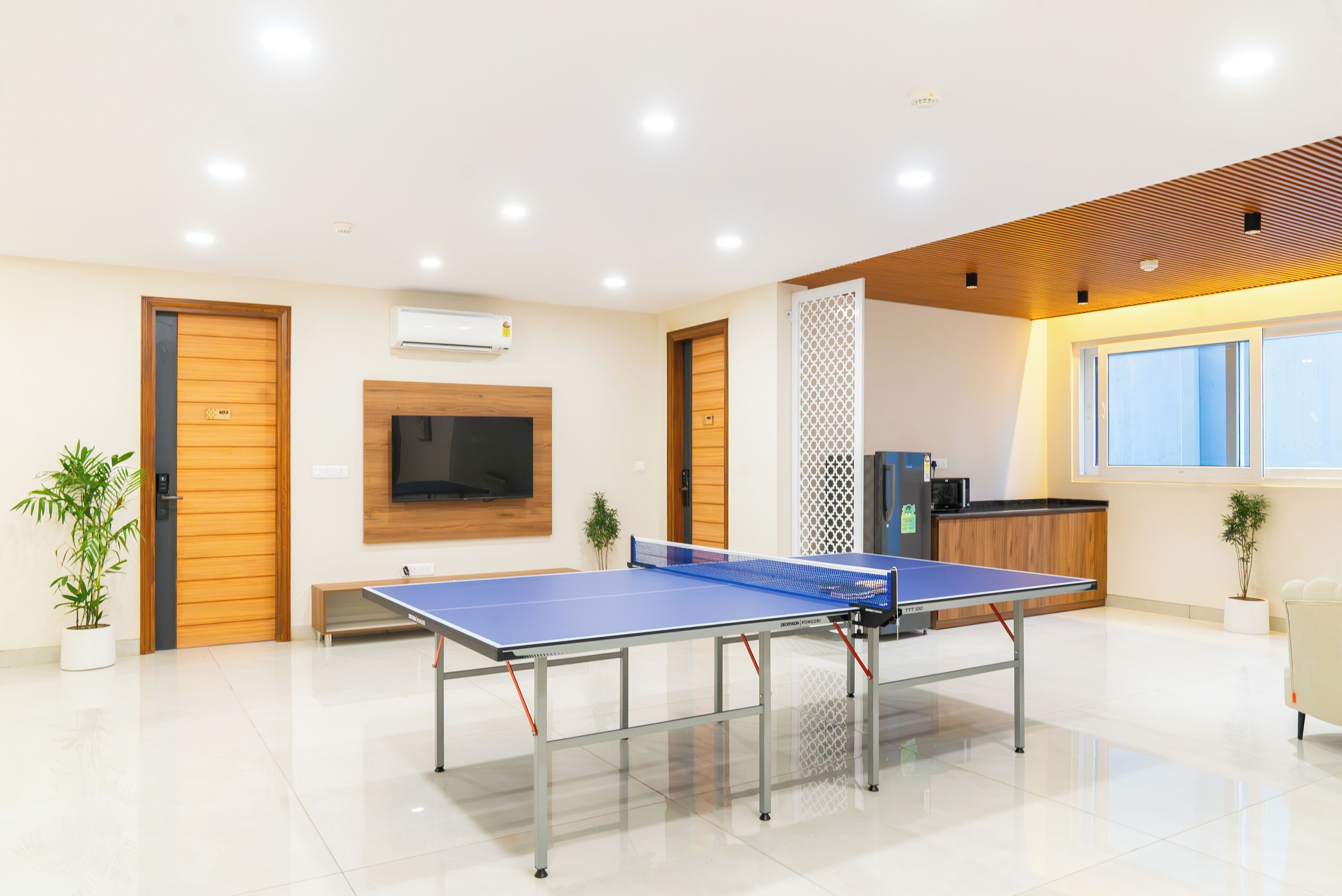 A modern room with a ping pong table, a TV, and a kitchenette.