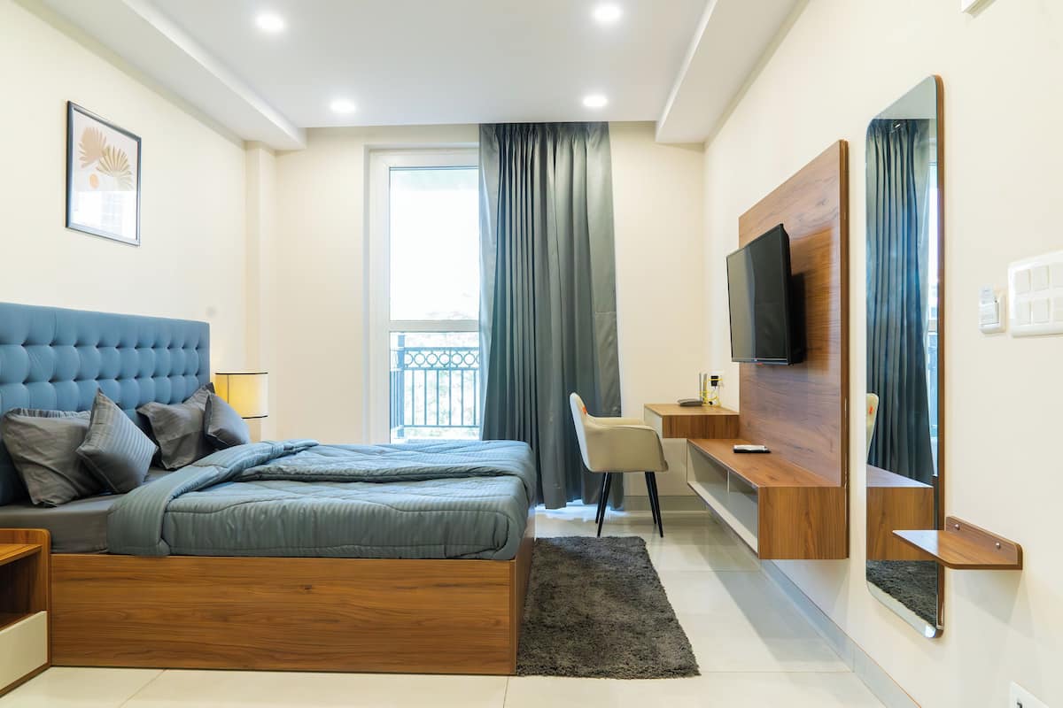 Quarto moderno com cama, escrivaninha, cadeira e televisão.