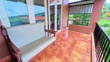 A balcony with a wooden bench, a glass door, and a view of a garden.