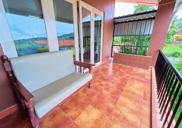 Ein Balkon mit einer hölzernen Bank, einer Glastür und Blick auf einen Garten.