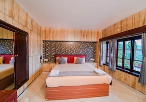 A bedroom with a large bed, wooden panel walls, a patterned headboard, and a window with curtains. - Silent Valley Farmstead by VOYE HOMES (Ooty)