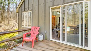 A wooden deck with a red chair and a propane tank, overlooking a forested area. - Steps to Jack Frost Ski Resort: Townhome w/ Decks (White Haven)