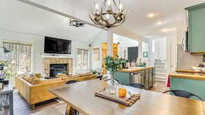 A spacious living room with a fireplace, a dining area with a wooden table, and a kitchen with green cabinets. - Steps to Jack Frost Ski Resort: Townhome w/ Decks (White Haven)