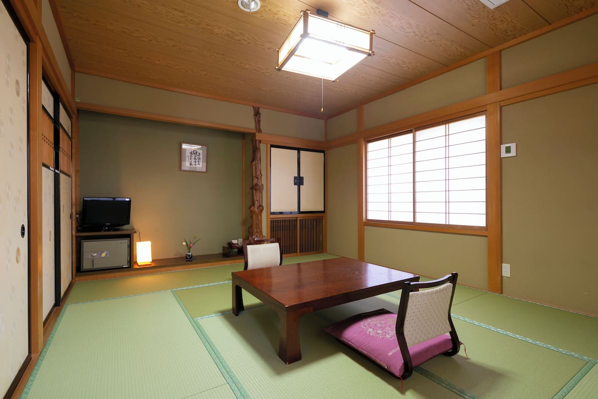 A traditional Japanese room with tatami flooring, a low table, and a television on a cabinet.