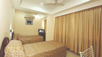 A hotel room with two beds, a ceiling fan, an air conditioning unit, a television, and a large window with curtains.