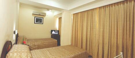 A hotel room with two beds, a ceiling fan, an air conditioning unit, a television, and a large window with curtains.