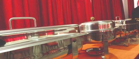 Carros tipo buffet con recipientes de metal, un telón de fondo rojo y una alfombra naranja.