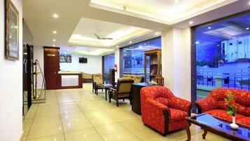 A hotel lobby with a reception desk, seating area, and large windows offering a view of the outside.
