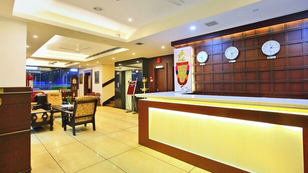 A hotel reception area with a reception desk, multiple clocks, a staircase, and a seating area with chairs. - Hotel Indraprastha Kayamkulam (Kayamkulam)