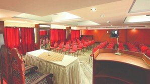 A conference room with rows of red chairs, a stage with a microphone, and a large table. - Hotel Indraprastha Kayamkulam (Kayamkulam)