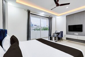 A modern hotel room with a large bed, a desk, a chair, a TV, and a balcony with a city view. - The Byke Business Hotel - Sector 29 (Gurugram)