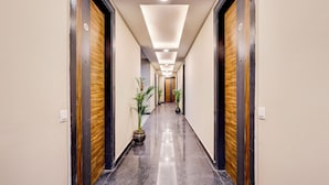 A long, narrow hallway with wooden doors on both sides, potted plants, and a shiny floor. - The Byke Business Hotel - Sector 29 (Gurugram)