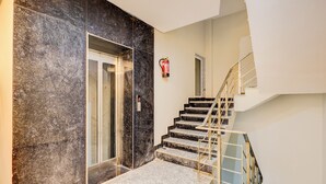 A modern interior with a marble wall, a glass elevator, and a staircase with a metal railing. - The Byke Business Hotel - Sector 29 (Gurugram)