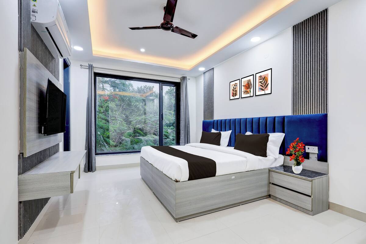 A modern bedroom with a large bed, a TV mounted on the wall, and a ceiling fan.