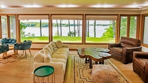 Un salon spacieux doté d’une grande fenêtre donnant sur un lac, et aménagé avec un canapé, des fauteuils et une table basse.
