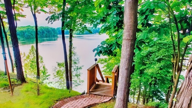 Une terrasse en bois mène à une petite construction également en bois, d’où l’on a vue sur un lac et une forêt.