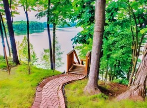 Une terrasse en bois mène à une petite construction également en bois, d’où l’on a vue sur un lac et une forêt.