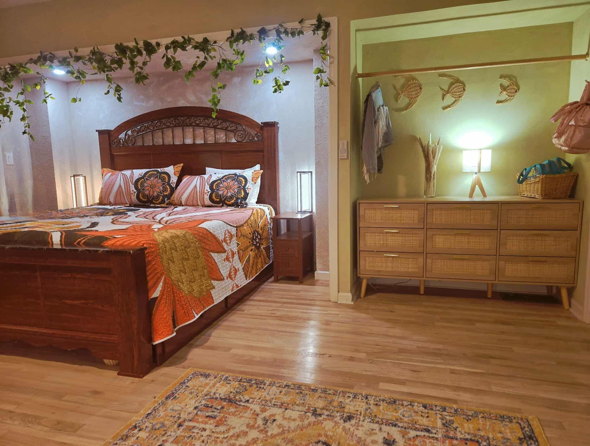 A bedroom with a wooden bed, a bedside table, a dresser, and a hanging plant.