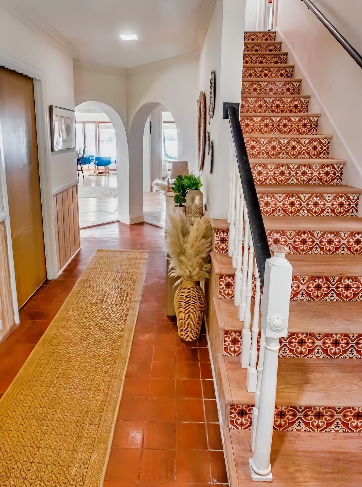 Un couloir avec un escalier décoré de motifs, un tapis et une plante.