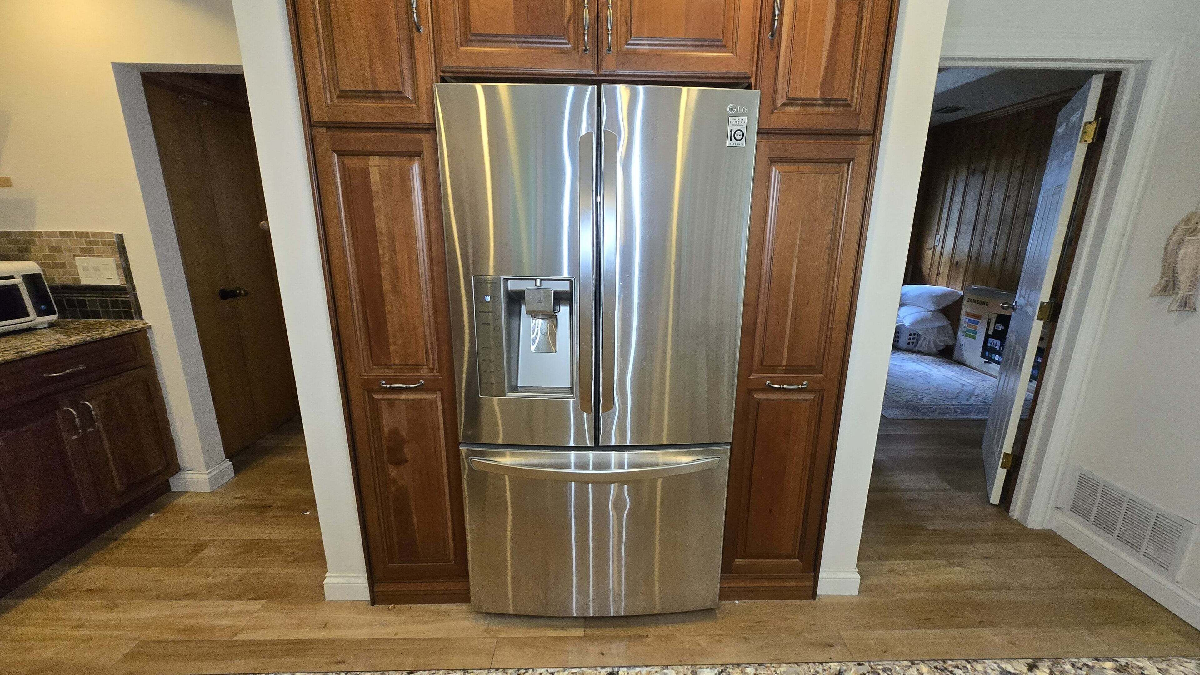A stainless steel refrigerator in a kitchen with wooden cabinets and a microwave on the counter.