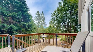 A wooden deck with a lounge chair and a small table, surrounded by trees.