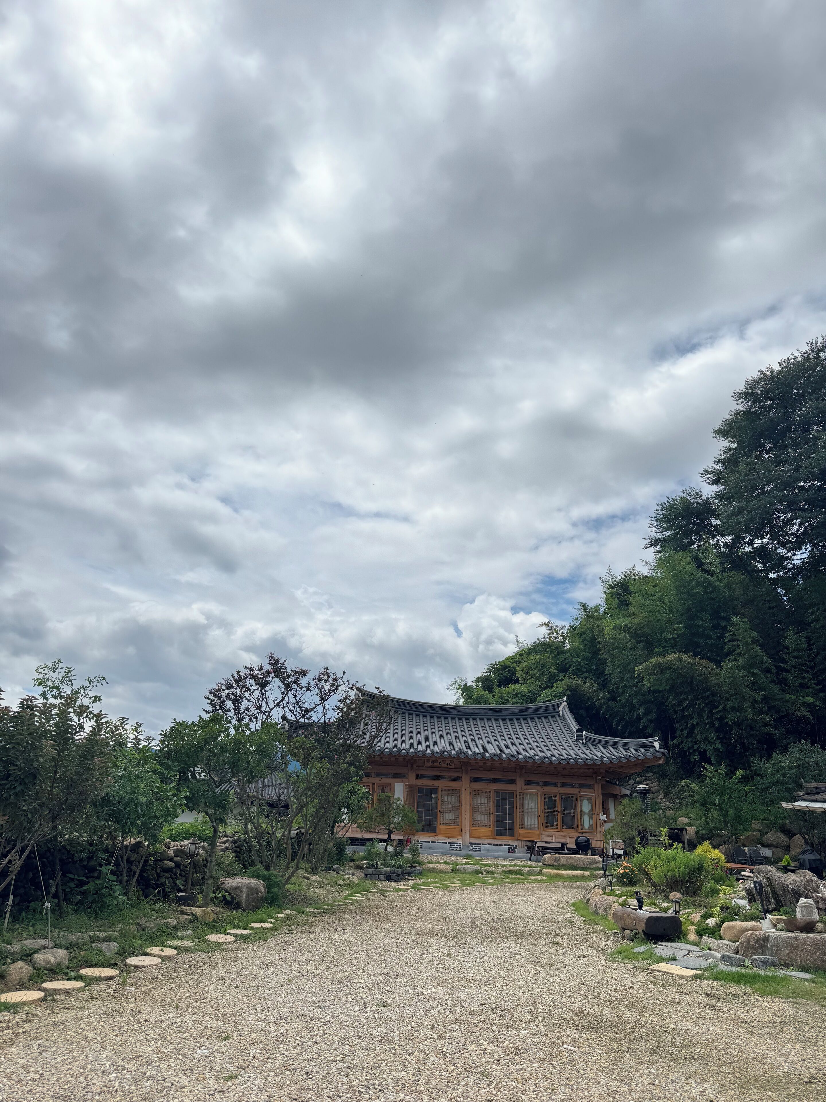 A traditional building with a tiled roof, surrounded by a gravel path and greenery.