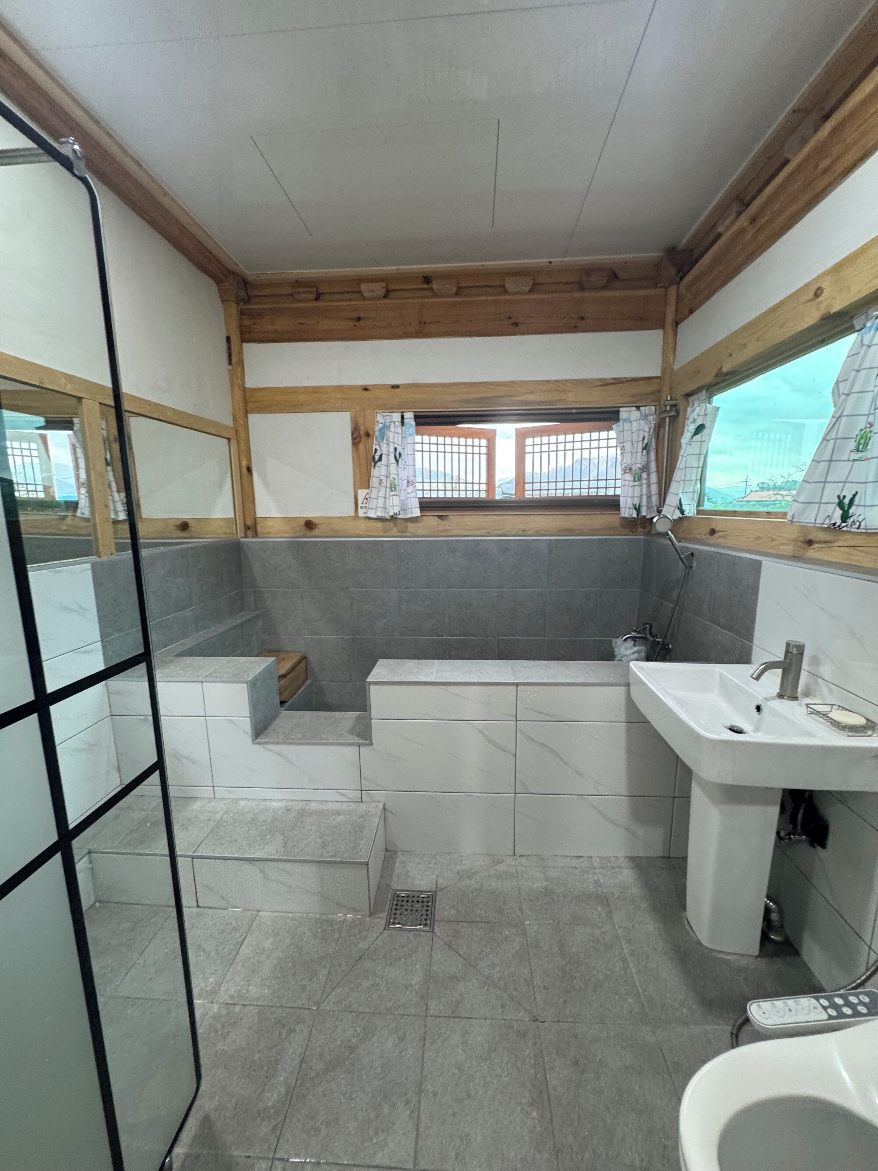Baño con bañera, lavabo e inodoro. Se aprecia una ventana con cortinas y vistas al exterior.