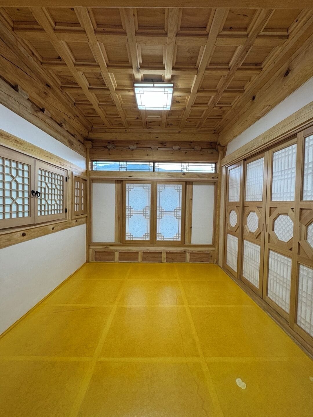 Una habitación japonesa tradicional con suelo de tatami, puertas correderas de madera con paneles de vidrio y un tragaluz.
