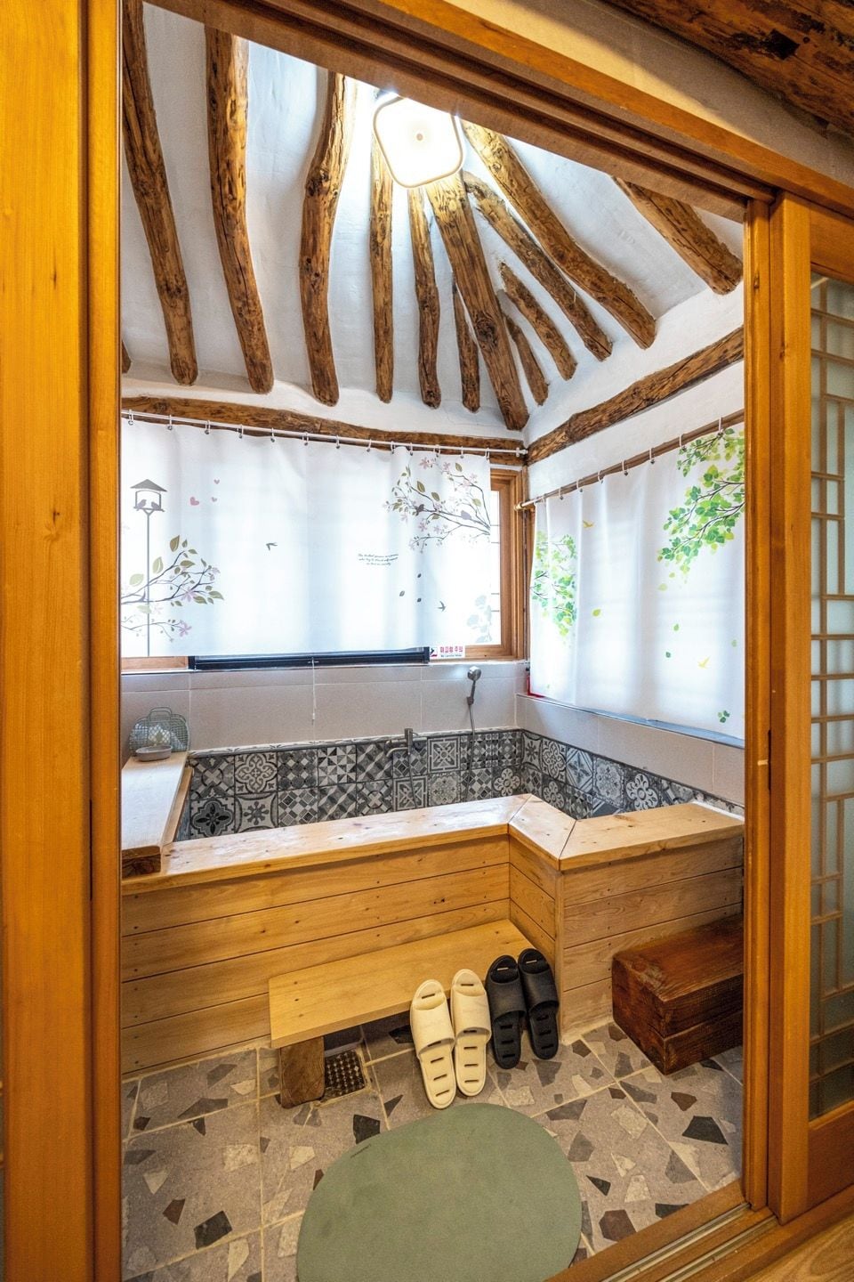Ein Holzhütten-Interieur mit einer steinplattenverlegten Badewanne, einer Bank und einem Paar Hausschuhe.