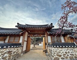 Puerta tradicional coreana con muros de piedra y techos de tejas, que da acceso a un patio.