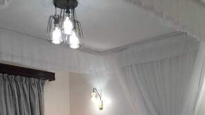 A neatly made bed with white linens and a teal throw, a bedside lamp, and a wall-mounted light fixture. - AZANIAHOMES (Nairobi)