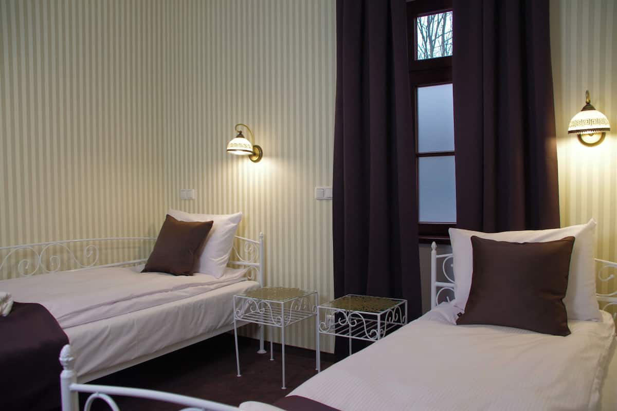 Habitación de hotel con dos camas individuales, una mesita y una ventana con cortinas.