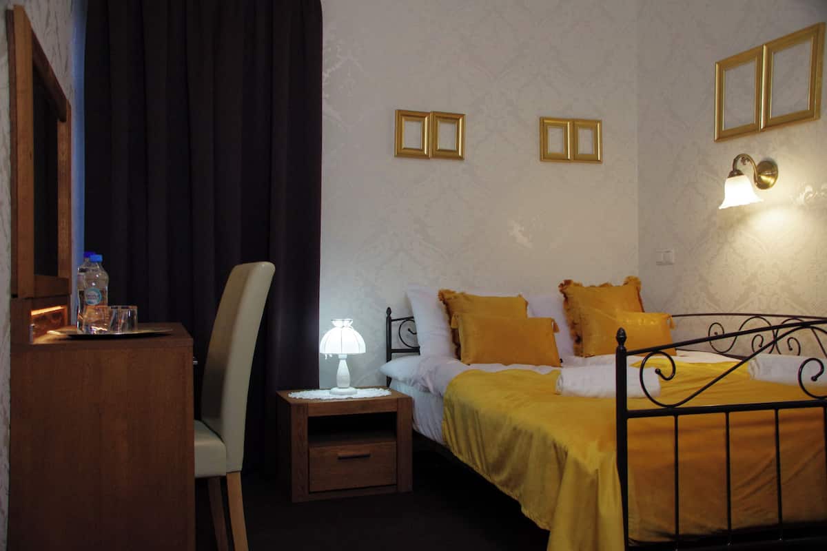 Una habitación de hotel con cama, sillón, mesita de noche con lámpara y pared decorada con marcos.