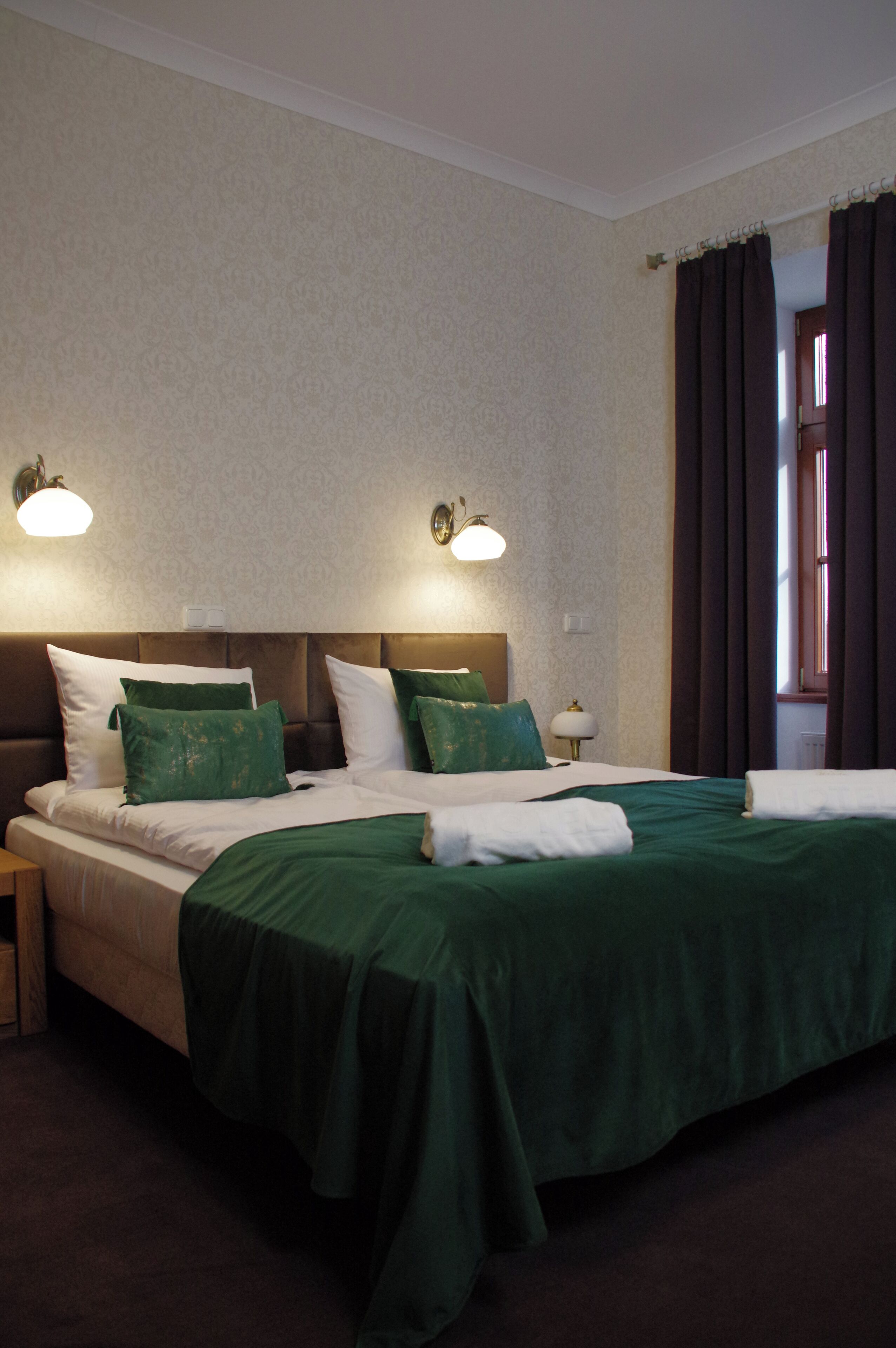 Ein Hotelzimmer mit einem großen Bett, einer grünen Bettdecke, zwei Wandlampen und einem Fenster mit Vorhängen.
